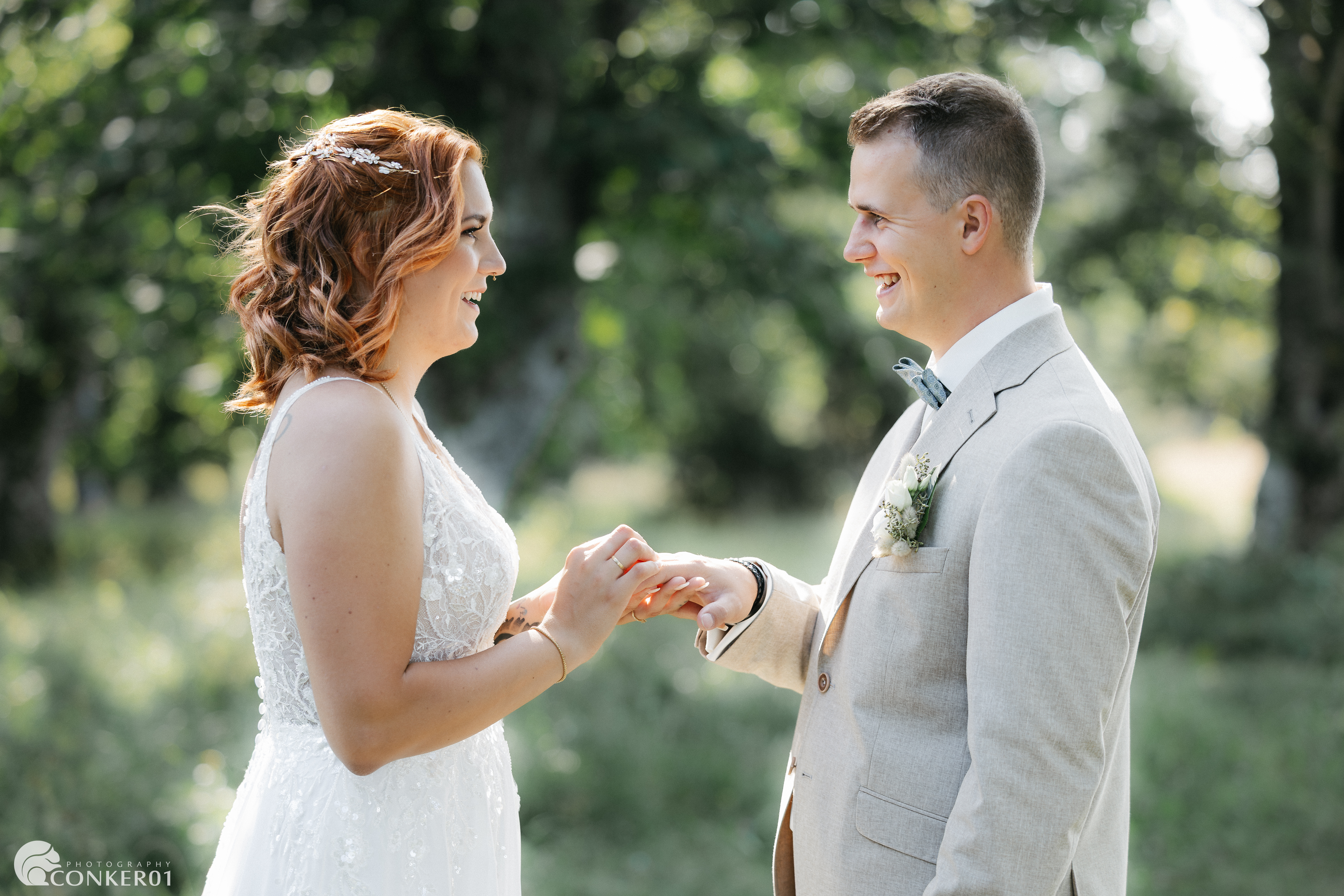 Braut steckt dem Bräutigam in der Natur den Ring an, beide lächeln sich intensiv an.