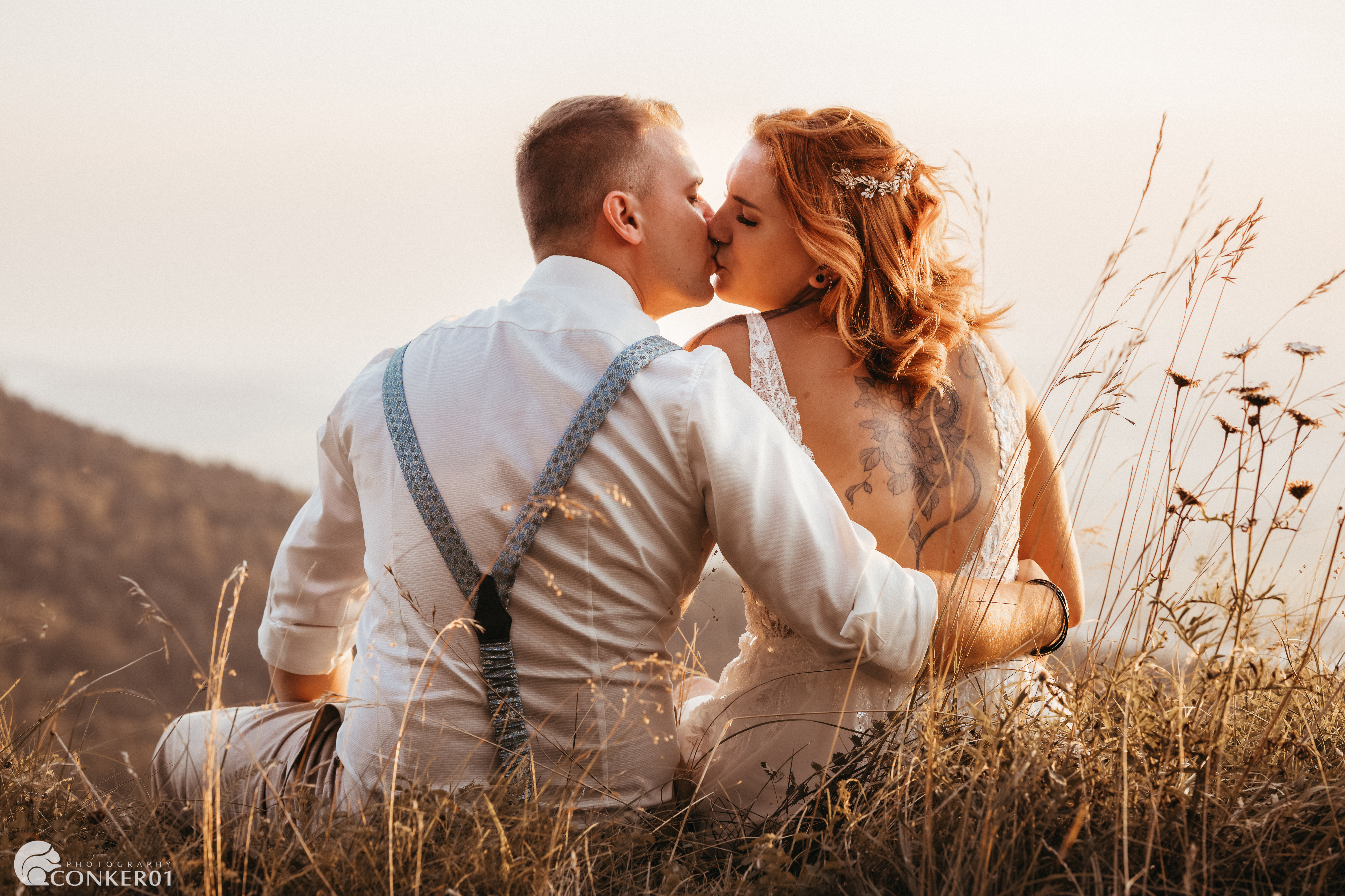 Küssendes Brautpaar im Sonnenuntergang, sitzend auf einer Wiese und den Abend gemeinsam genießend.
